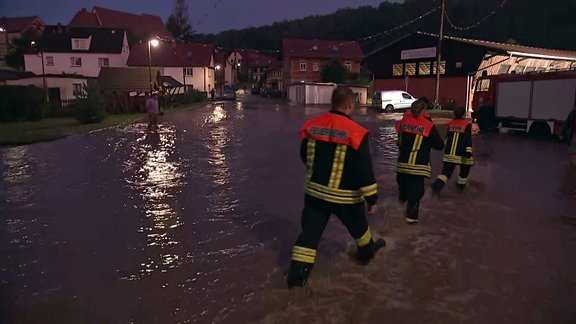 Drei Feuerwehrleute laufen durch eine überflutete Straße in Stadtroda.