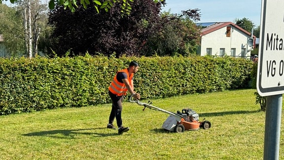 Mann in Warnweste mäht Rasen