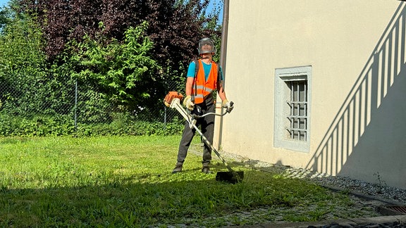 Mann in Warnweste und mit Schutzhelm arbeitet mit Rasentrimmer