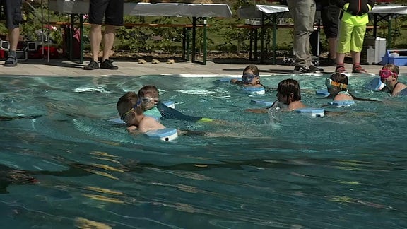 Kinder schwimmen in einem Schwimmbecken.