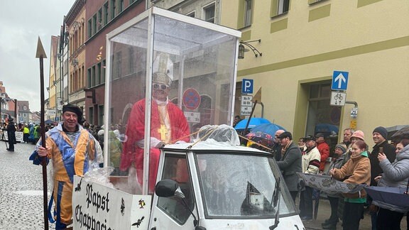 Eine Vespa umgebaut als "Papamobil" mit einem verkleideten Mann drin als Papst