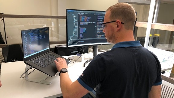 Ein Mann steht an einem Computer, auf dem ein Software-Code zu sehen ist.