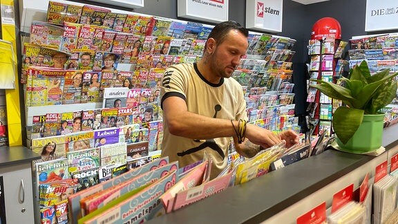 Michél Schulze sortiert Zeitschriften im Kiosk.