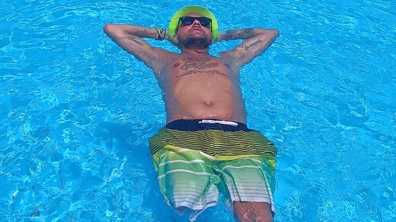Michél Schulze mit Badehose und Sonnenbrille im Schwimmingpool.