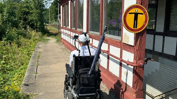 Ein Mann im Rollstuhl fährt an einem Treppenaufgang vorbei. Ein Schild mit dem Piktogramm eines Menschen ist dort angebracht.