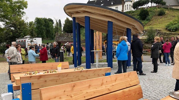 Menschen stehen vor einem Unterstand aus Holz.