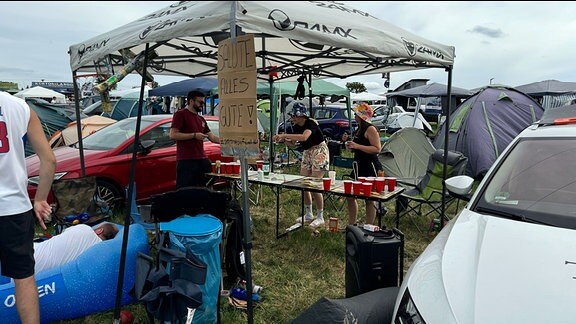 Eine Gruppe Festivalbesucher machen es sich unter einem Regenzelt gemütlich