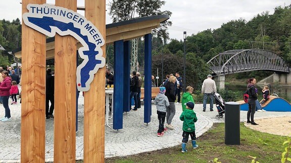 Ein Schild mit Aufschrift "Thüringer Meer", im Hintergrund eine Brücke.