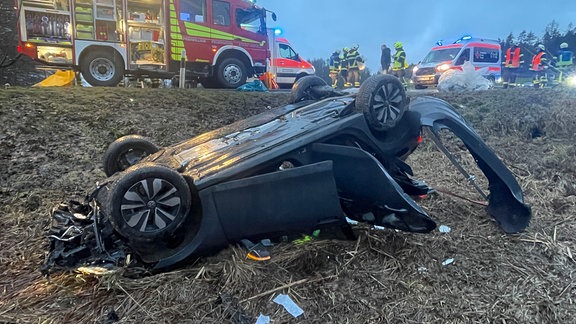 Schwarzes Autowrack liegt neben der Straße auf dem Dach, Feuerwehrfahrzeug auf der Straße