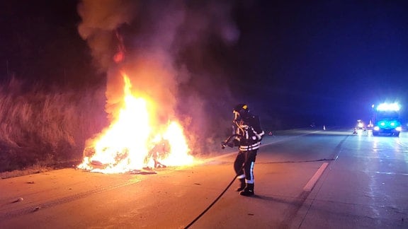Ein Feuerwehrmann steht neben einem brennenden Auto auf einer Autobahn.