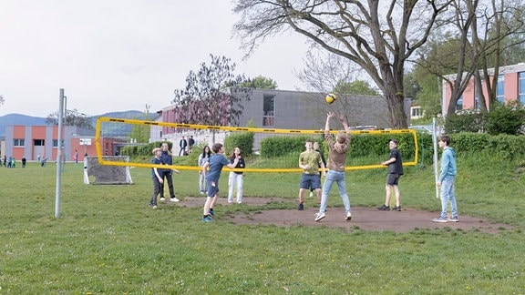 Kinder spielen auf einer Wiese Volleyball. 