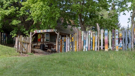 Bunt bemalter Zaun mit einem Tor, auf dem "Schulgarten" steht, auf einer Wiese.