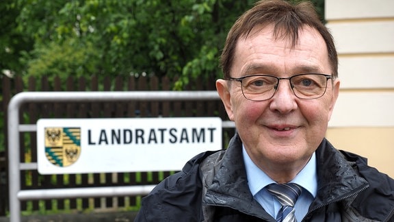 Karlheinz Frosch vor dem Landtratsamt im Kreis Saalfeld-Rudolstadt. Er trägt Brille, Schlips und eine wattierte Jacke.