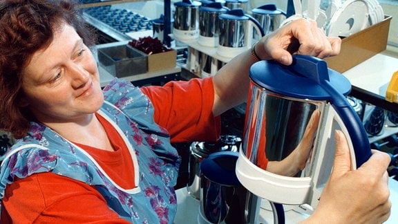 Eine Frau in einer Werkstatt hält eine Wasserkocher hoch