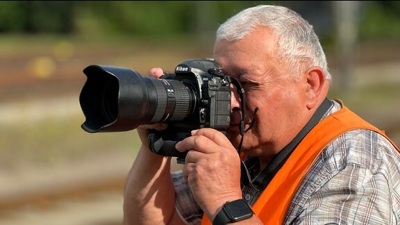 Ein Mann mit Warnweste schaut durch eine Fotokamera.