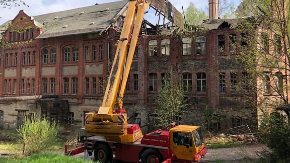 Ein Kran hebt ein Dachstück von einem zerfallenen Fabrikgebäude.