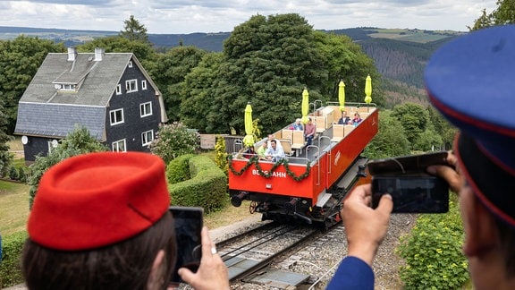 Menschen in historischen Bahnuniformen fotografieren vor Beginn des Jubiläumsfests 100 Jahre Bergbahn Oberweißbach den ankommenden Cabriowaggon auf der Güterbühne. 