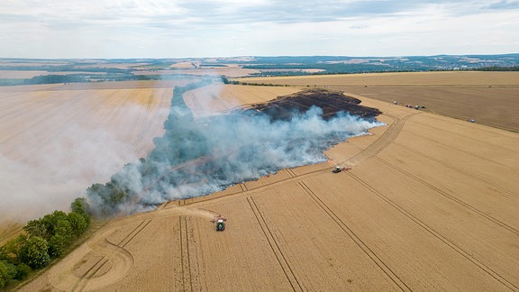 Luftaufnahme: Zwei Traktoren pflügen einen Brandschutzstreifen um einen Brandherd