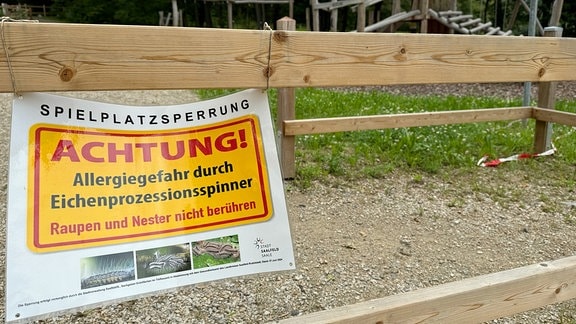 Absperrung auf einem Spielplatz mit dem Schild: "Spielplatzsperrung -- ACHTUNG Allergiegefahr durch Eichenprozesionsspinner -- Raupen und Nester nicht berühren."