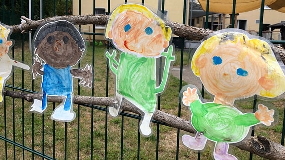 Papierfiguren mit Kindern hängen an einem Zaun.