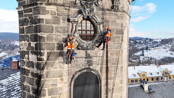 Zwei Kletterer befästigen ein Netz an einem Schlossturm.