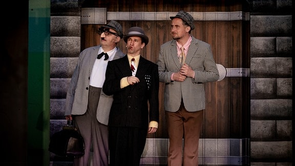 Drei Männer stehen auf einer Theaterbühne.