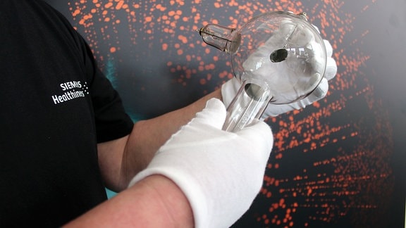 Röntgen-Röhre wird von einer Person mit beiden Händen gehalten. Dabei trägt diese Person weiße Handschuhe.