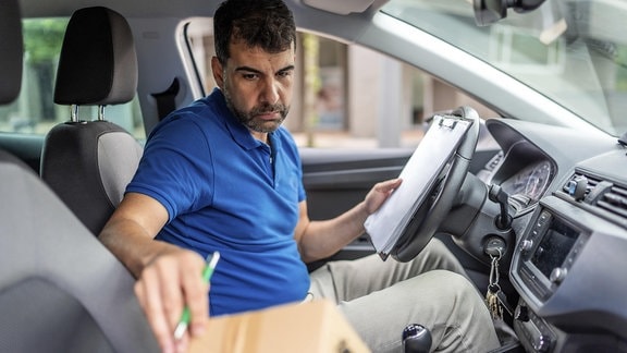 Seitenansicht eines professionellen Zustellers, der Pakete in einem Auto überprüft