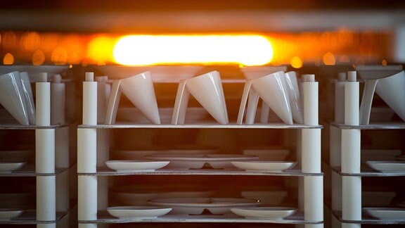 Teller, Tassen und Schalen laufen in der Produktion einer Porzellanfabrik durch einen Ofen