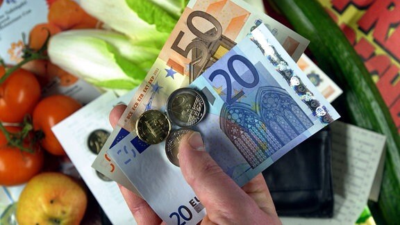 Lebensmittel und eine Hand mit Euro-Scheinen