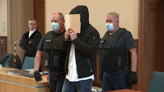 Der Angeklagte verbirgt sein Gesicht im Gerichtssaal hinter einer Mappe.