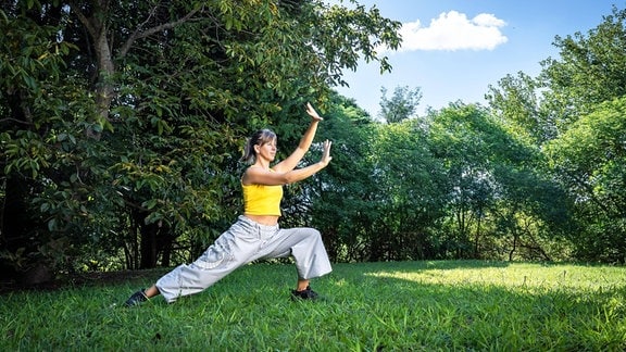 Eine Frau übt Qigong in einem Park.