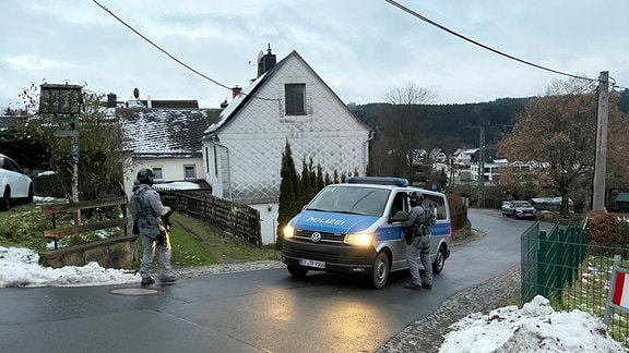Bewaffnete und vermummte Polizisten und ein Polizeifahrzeug stehen während einer Razzia auf einer Straße in Bad Lobenstein.