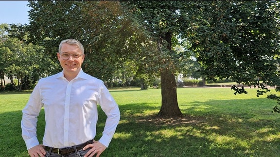 Der FDP-Politiker Robert-Martin Montag steht in einem Park vor einem Baum. 