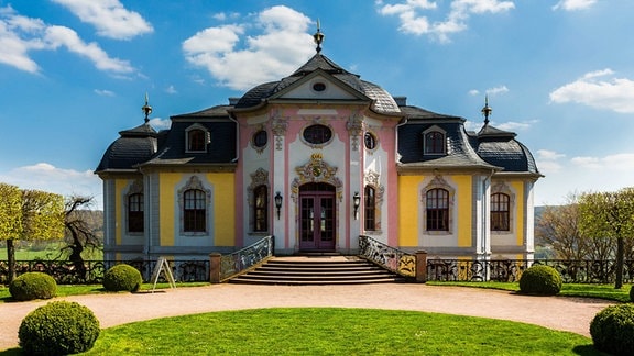 Dornburger Schlösser, Rokoko-Schloss: ein gebäude mit rosa-gelber Fassade und rundem Dach in einem Garten, im Hintergrund blauer Himmel