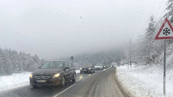 Mehrere Autos fahren auf einer verschneiten Straße.