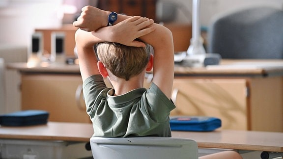 Ein Schuljunge sitzt mit erhobenen Armen im Unterricht.