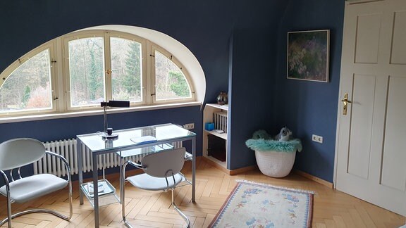 ein Schreibtisch mit zwei Stühlen steht vor einem Fenster in einem Zimmer mit dunkelblau gestrichenen Wänden.