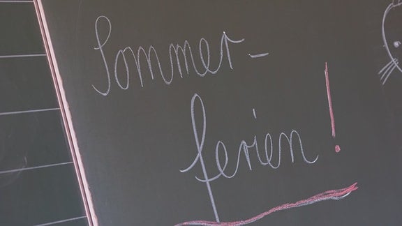 An einer Tafel in einer Schule steht "Sommerferien!" geschrieben.