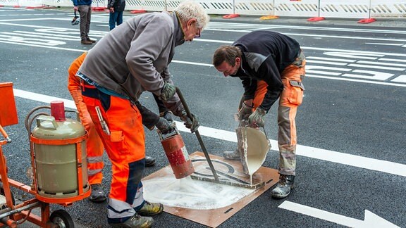 Arbeiter bringen neue Fahrbahnmarkierungen auf einer Straße auf.