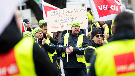 Ein Teilnehmer einer Verdi-Demonstration steht mit einem Schild mit der Aufschrift «Nicht der Streik gefährdet den PNV, sondern der Arbeitgeberverband» während einer Kundgebung in der Innenstadt von Hannover.