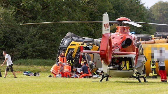Rettungskräfte versorgen einen Verletzten, ein Betonmischer liegt auf der Seite, ein Hubschrauber
