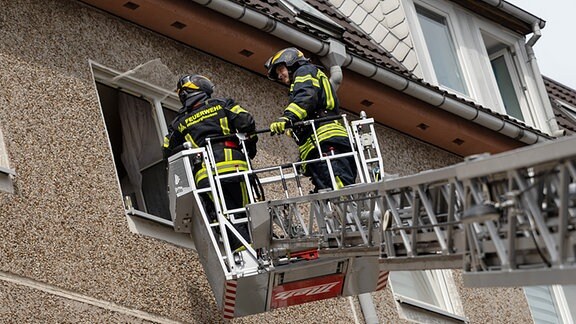 Zwei Feuerwehrmänner auf ausgefahrener Drehleiter vor Wohnhaus