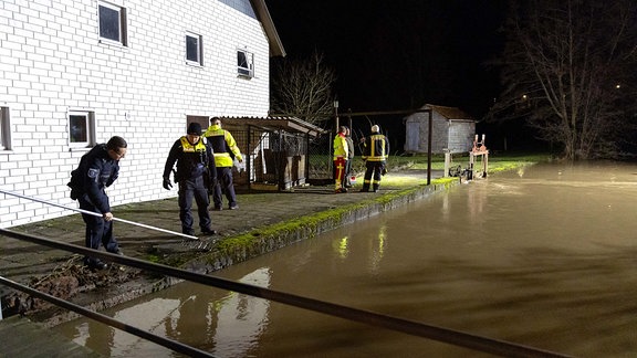 Polizisten und Feuerwehrleute stehen vor einem Haus an einem Fluss