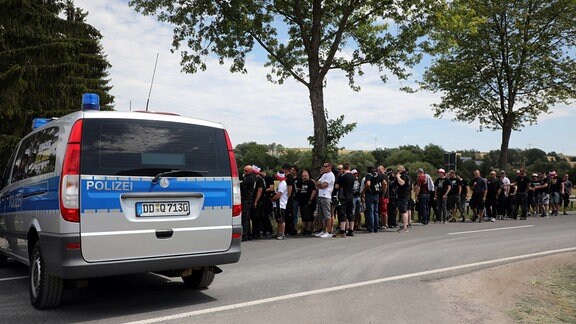 Teilnehmer eines Rechtsrock-Festivals stehen auf dem Weg zum Veranstaltungsgelände in einer Schlange vor der Einlasskontrolle der Polizei