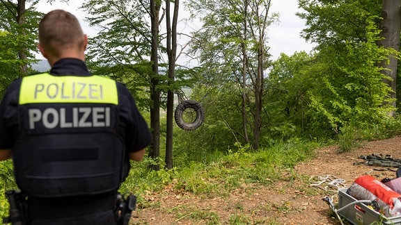 Eine Reifenschaukel am Hang im Wald, davor steht ein Polizist