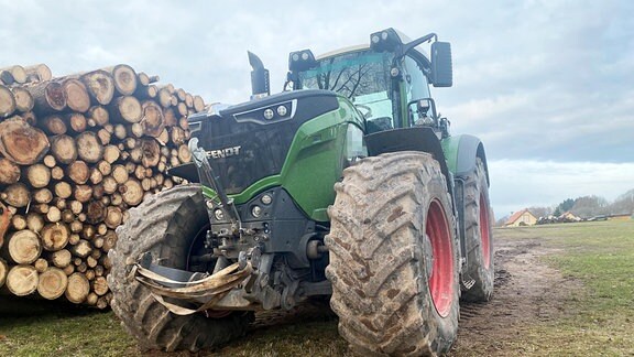 Ein Traktor neben einem Holzstapel.