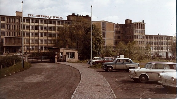 Foto eines langgezogenen fünfetagigen Gebäudes, davor stehen Autos.