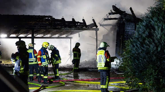 Feuerwehrleute stehen in der Nacht vor einem abgebrannten Haus.