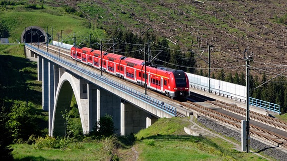 Ein roter Zug fährt über eine Brücke.